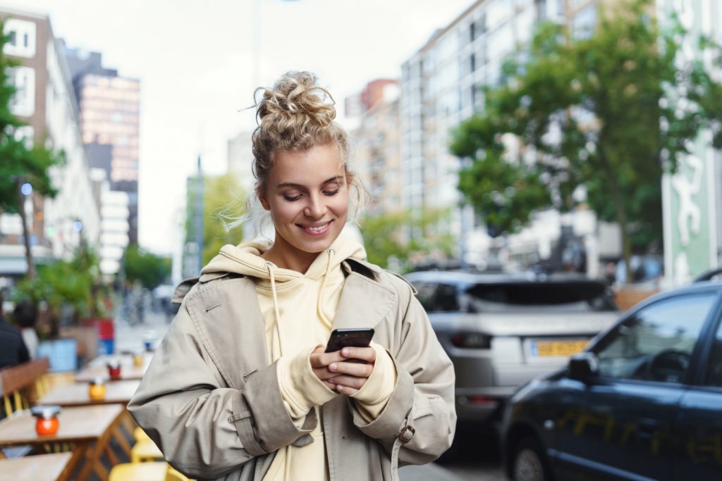 Uśmiechnięta piękna blond dziewczyna używa telefonu komórkowego.